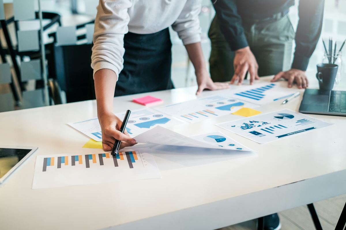 Two people marking up printed charts and reports on a desk