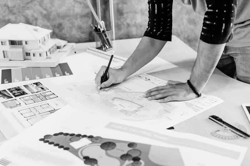 Hands drafting architectural plans beside a building model