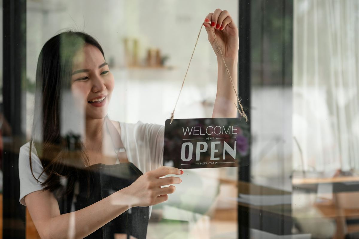 A shop owner hanging a Welcome, Open sign in her window